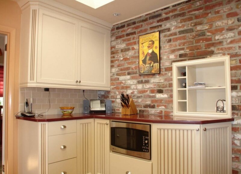 A cream-colored kitchen with an exposed red brick accent wall and deep red countertops