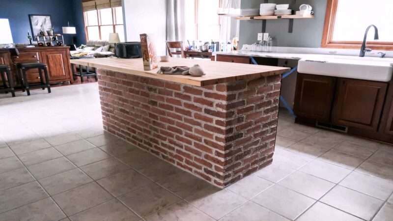 A brick-based kitchen island with a wooden countertop in an open-concept space