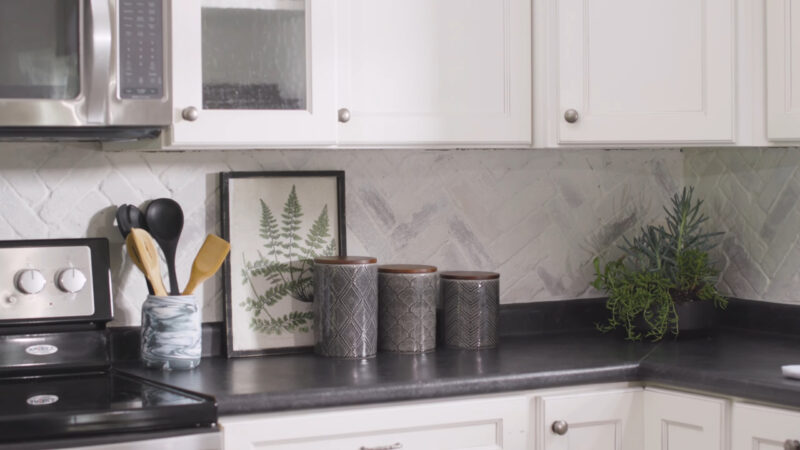 A whitewashed brick backsplash in a modern kitchen with black countertops and decorative accents