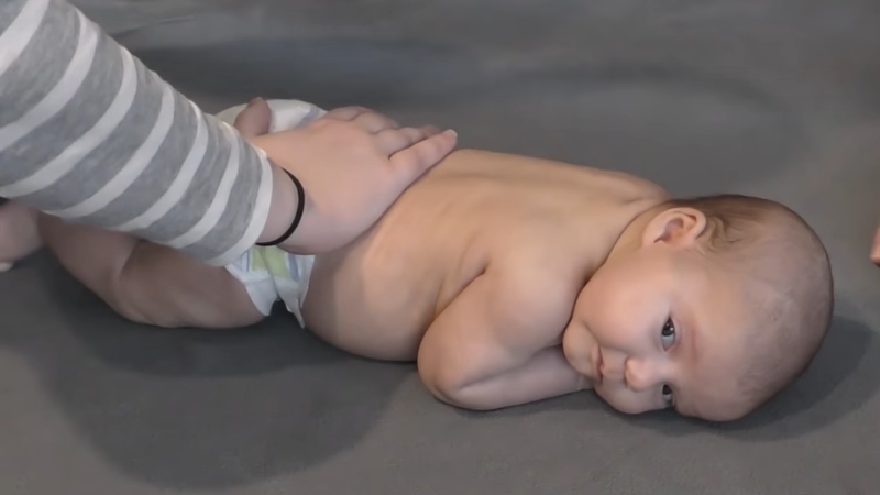 A Baby Lying on Their Stomach During Tummy Time with A Hand Supporting Their Back