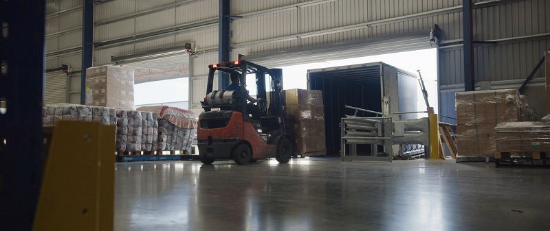 Forklift loading goods into a truck inside a warehouse, emphasizing logistics as a key component of business expansion
