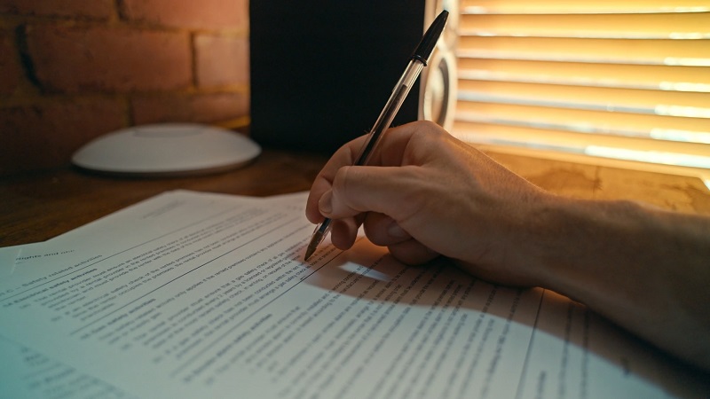 A hand holding a pen and signing official business documents, highlighting legal compliance during expansion