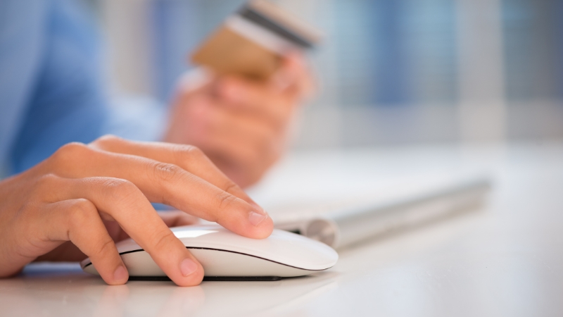 Person clicks a mouse while holding a credit card, showing first-click linked to buying
