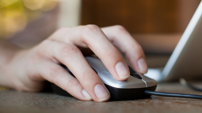 A person clicks a wired computer mouse next to a laptop, representing the concept of first-click attribution