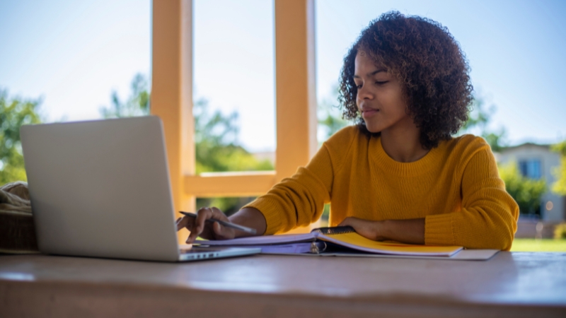 A student in STEM studies at a laptop with notes and a binder open on the table