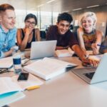 A group of students in STEM work together at a table with laptops, books, and notes during a study session