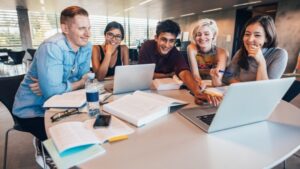 A group of students in STEM work together at a table with laptops, books, and notes during a study session