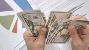 A person counting dollar bills over financial charts, representing small business cash flow management