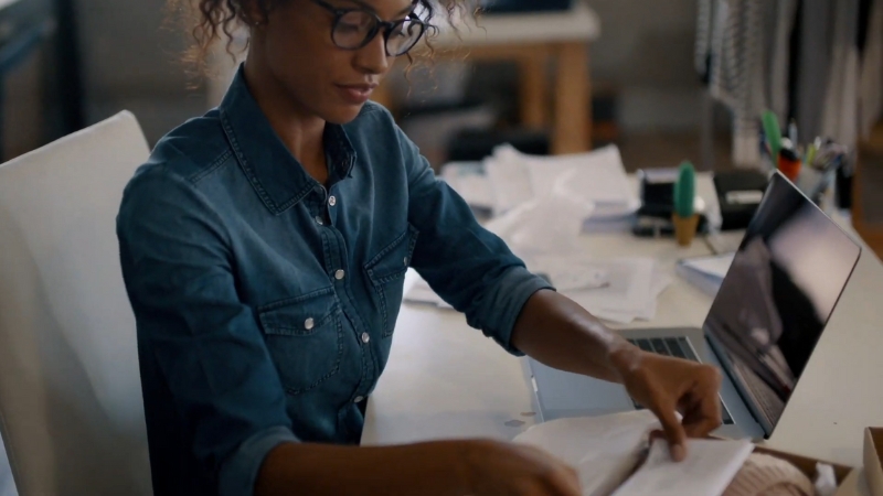 A woman working at a desk with papers and a laptop, organizing business finances and managing cash flow tools