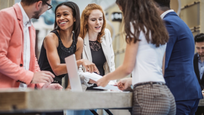 A group of people gathered at an event table, engaging in conversation and exchanging papers
