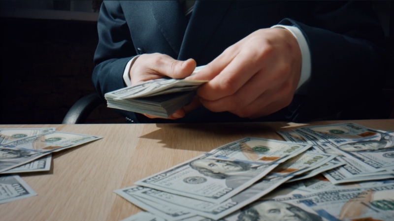 A person in a suit counting stacks of hundred dollar bills on a desk