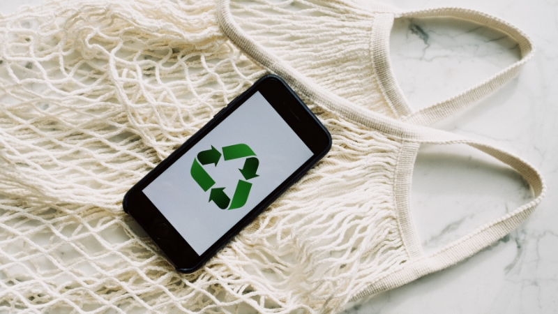 A reusable cotton tote bag with a phone displaying a green recycling symbol on the screen