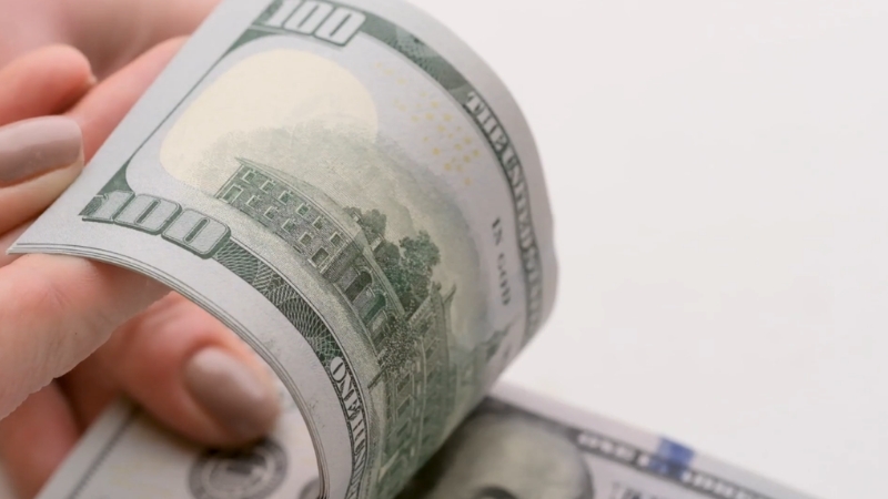 A person flipping through a stack of 100 dollar bills, symbolizing cash flow management