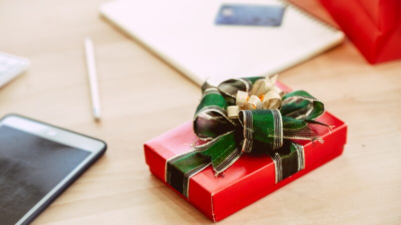 A wrapped gift box sits on a desk next to a tablet and notebook