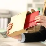 A business professional opens a box with a branded gift on a desk in an office setting