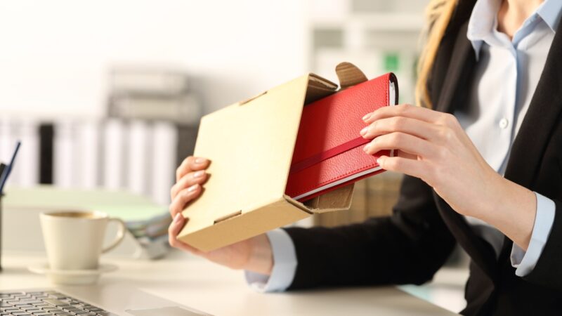A business professional opens a box with a branded gift on a desk in an office setting