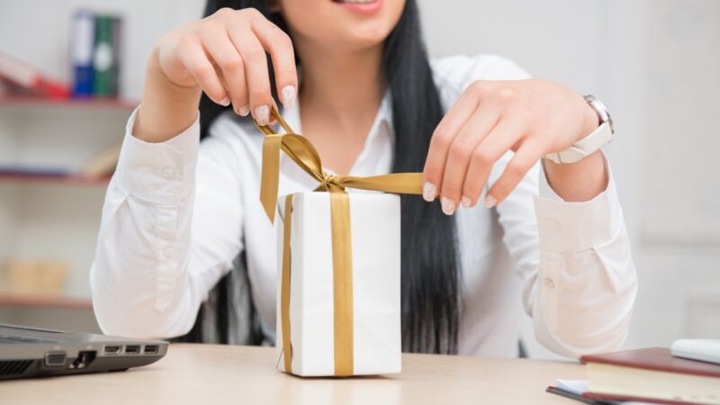 A woman ties a ribbon on a gift box on a desk, showing personalized branded gifting