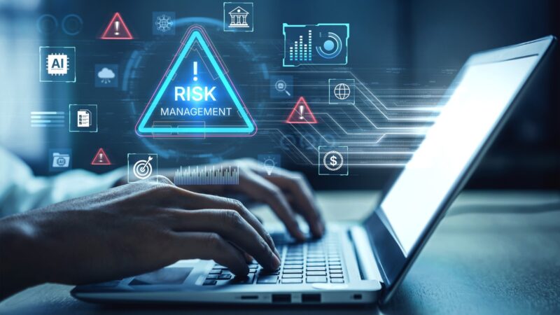 Risk automation dashboard on a laptop shows digital risk alerts and business review data