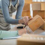 Two small business workers prepare cardboard boxes for customer orders.