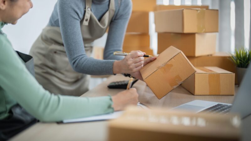 Two small business workers prepare cardboard boxes for customer orders.