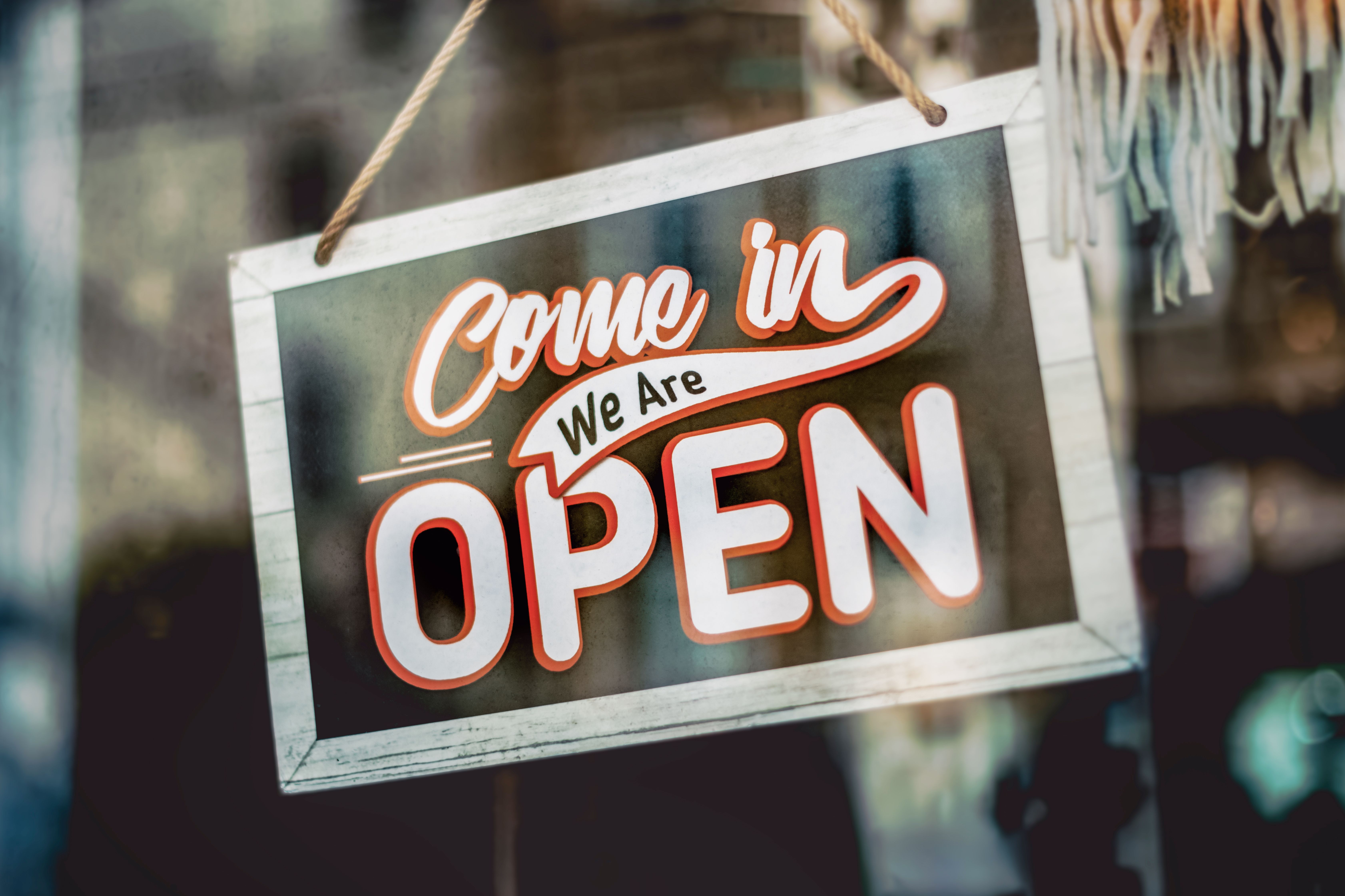 Welcoming 'Come in, We Are Open' sign hanging on the glass window of an urban shop